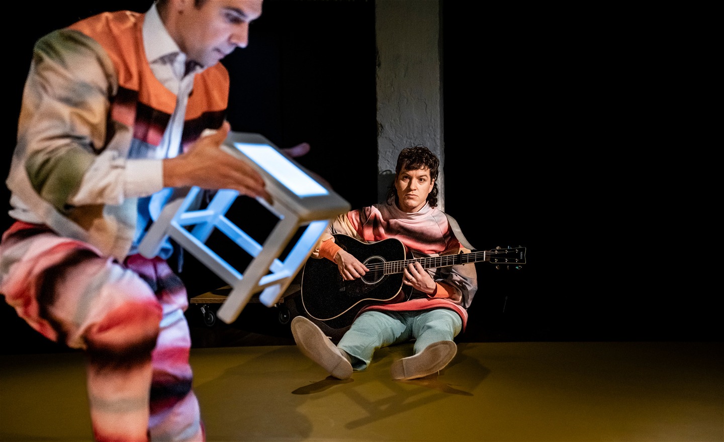 Niklas balanserar en självlysande pall, Martin sitter i bakgrunden med sin gitar.