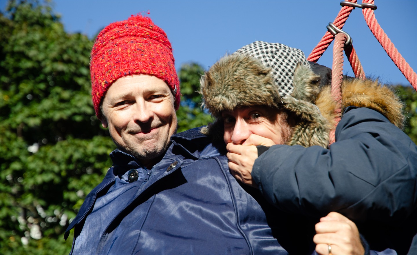 Två vinterklädda skådespelare kikar på oss i en klätterställning.