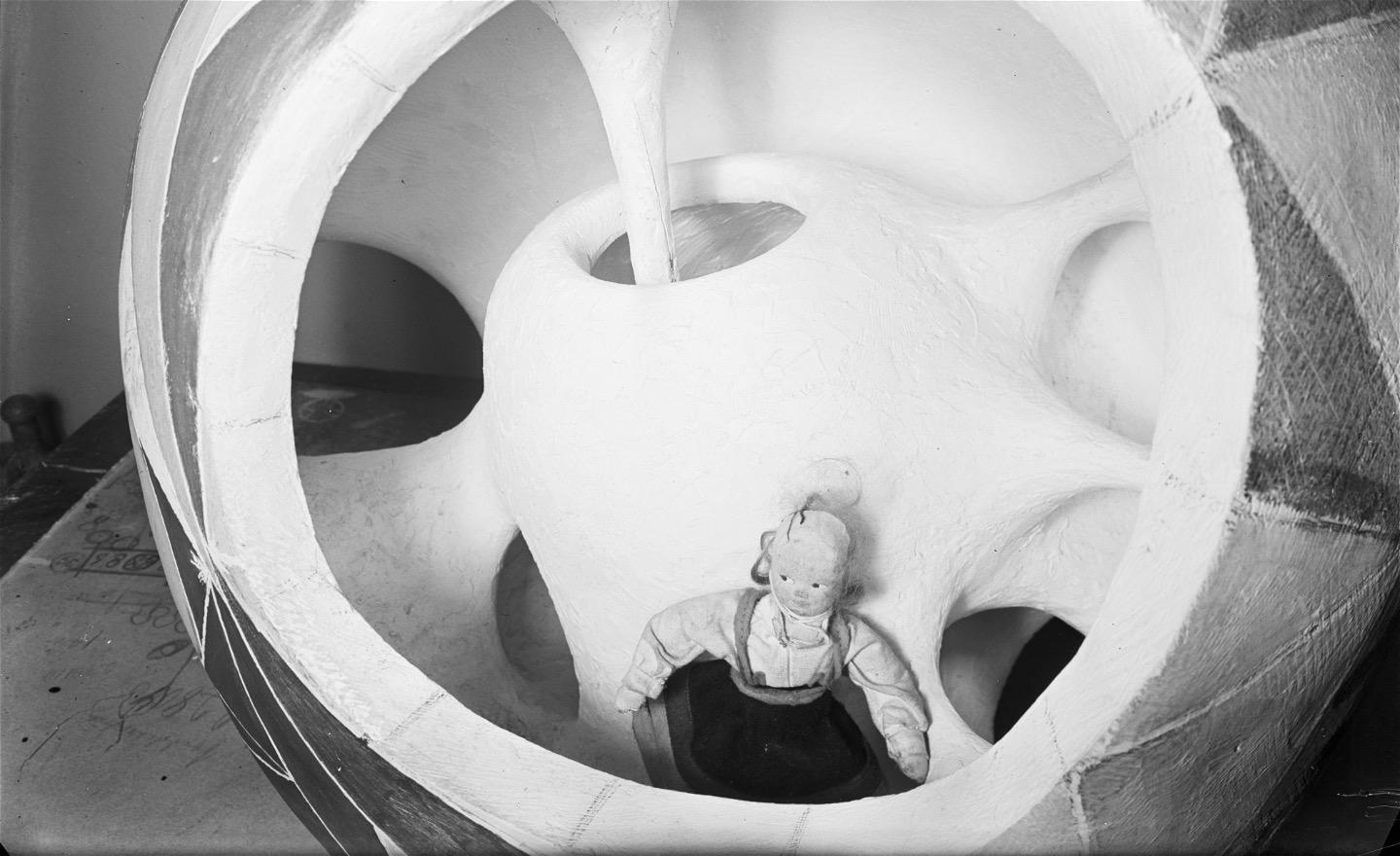 En docka sitter i en rund lekskulpturen med många hål som barn kan klättra ut och in ur.