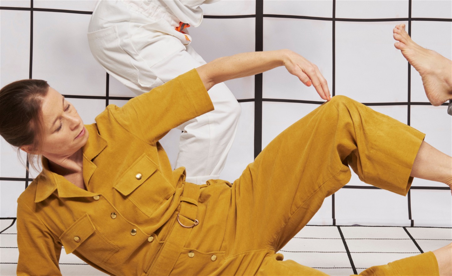 Åsa i gul kostym, formar kroppen till ett B, en skymtar höger i bild.