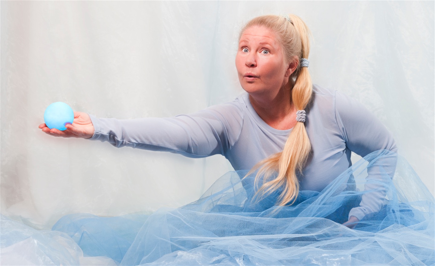 Person som sitter bland blått tyg och dansar med en boll i handen