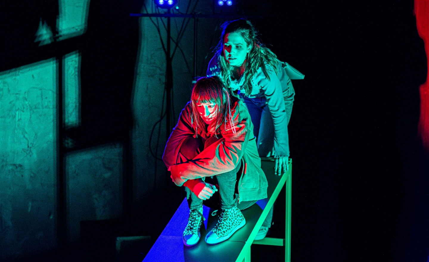 En tjej sitter hopkrupen högst upp på en ramp. En annan tjej står bakom henne. 