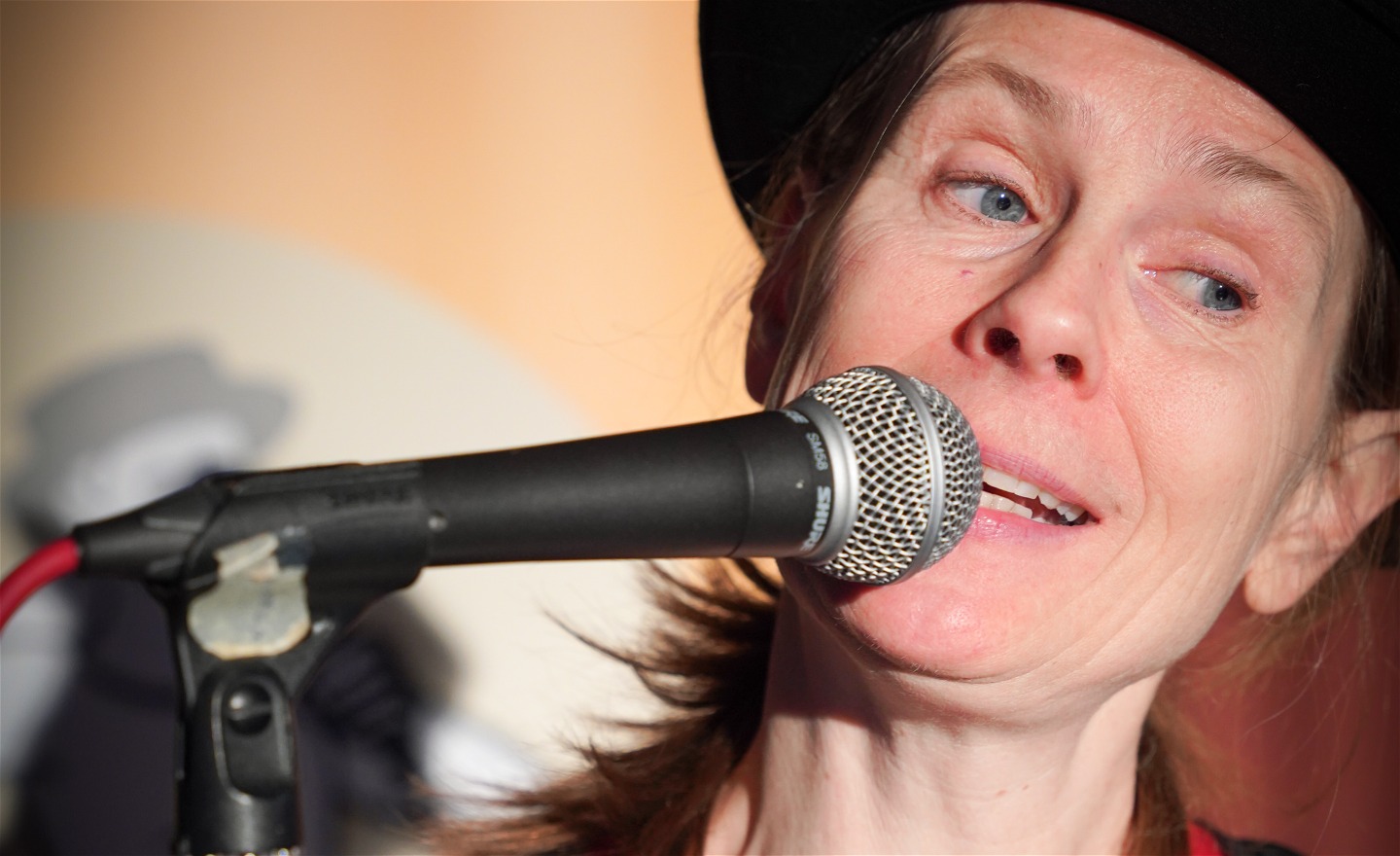 Närbild på Micaela som har en svart hatt pratar i en mikrofon och ser snäll