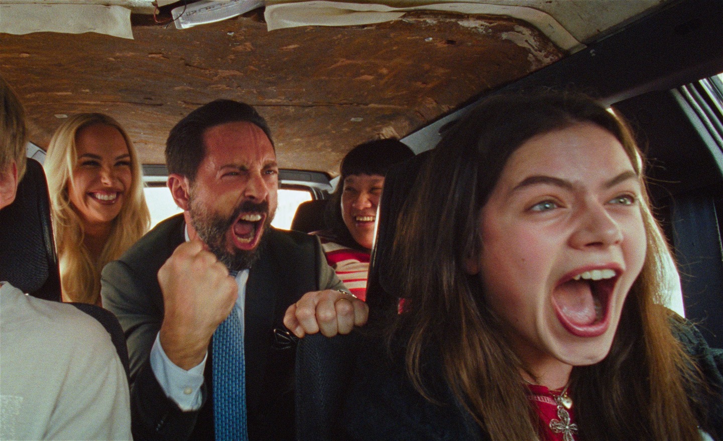 Tre unga kvinnor och två unga män sitter i en bil. De skrattar och skriker.  