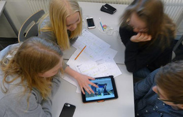 Elever sitter runt ett bord och arbetar med bildmanus och ipad sett uppifrån.