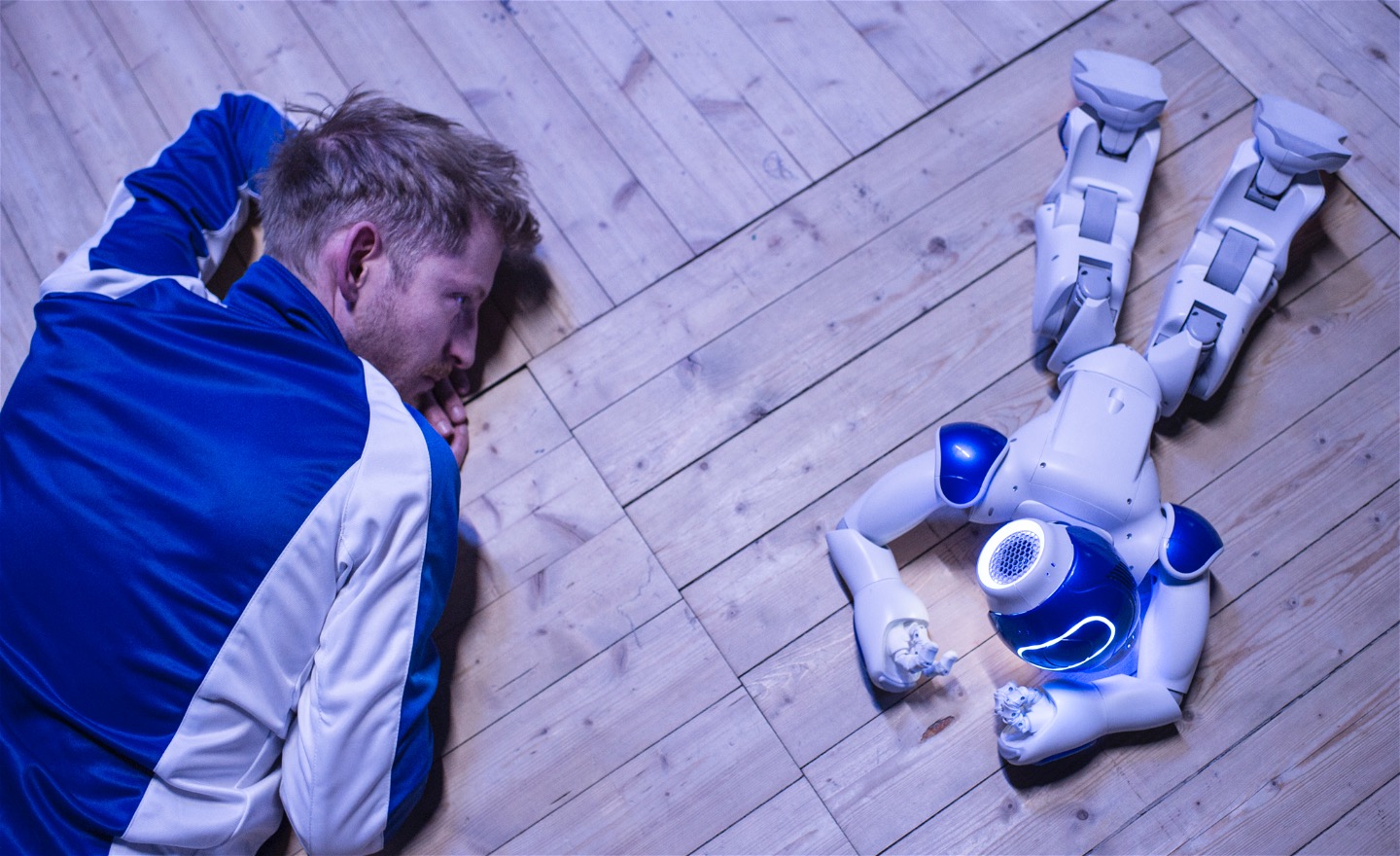 En robot ligger på ett dansgolv bredvid en dansare.