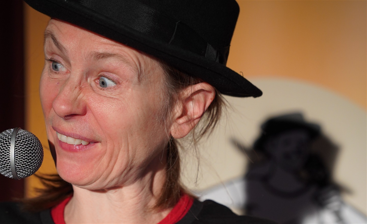 Micaela har en svart hatt och gör en rolig grimasch framför en mikrofon