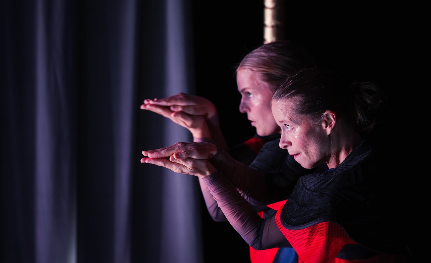 Två personer står profil på en scen och håller ihop händerna som en näbb.