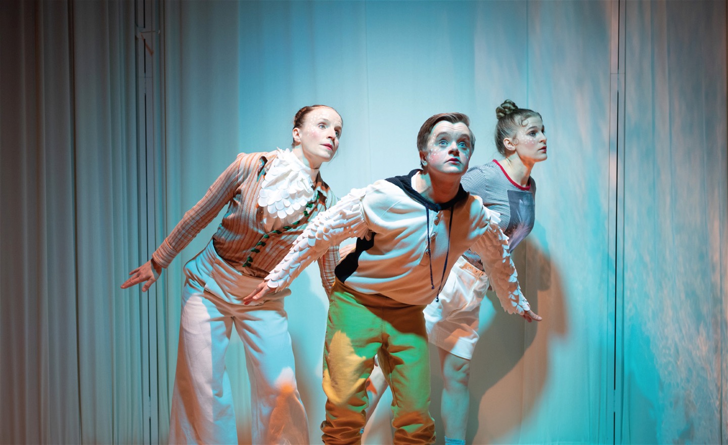 Tre dansare spanar ut från scenen med bakåtsträckta armar.