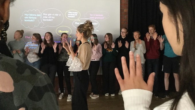 Elever står i ring runt en pedagog och håller upp sina handflator framför sig.