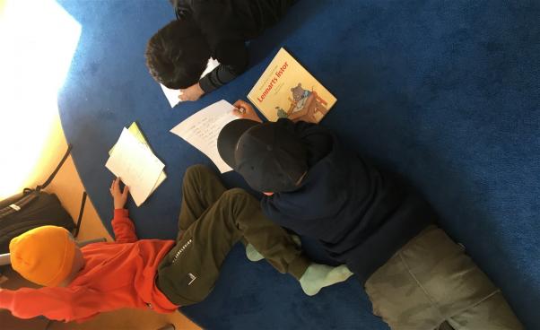 Barn läser och skriver liggande på mattan.