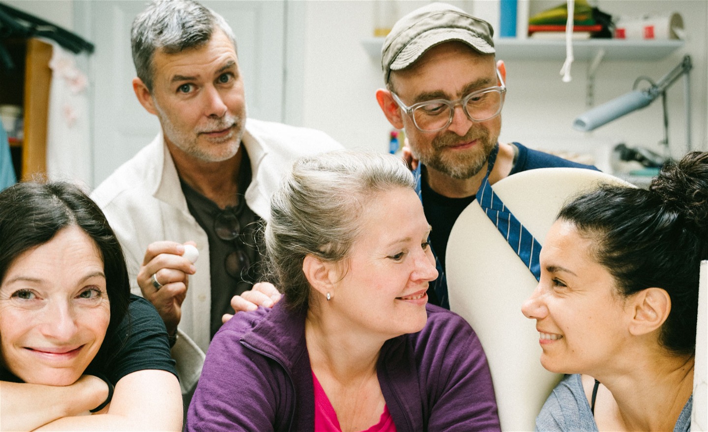 5 personer står i en kostymverkstad. Två personer tittar in i kameran och tre personer tittar på varandra.