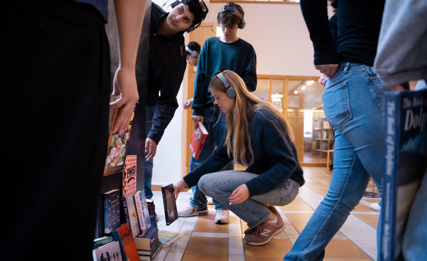 Flera personer med hörlurar bygger en skulptur av böcker