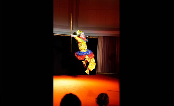 Apkungen gör ett akrobatiskt hopp på scenen med en trästav i handen,
