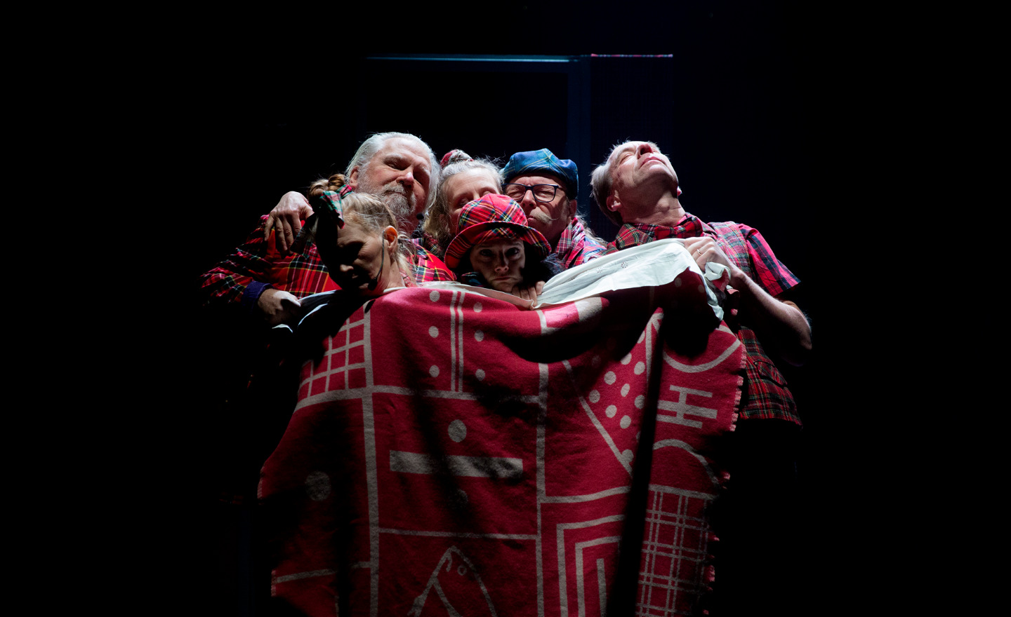 Skådespelare trängs i en säng under samma täcke.