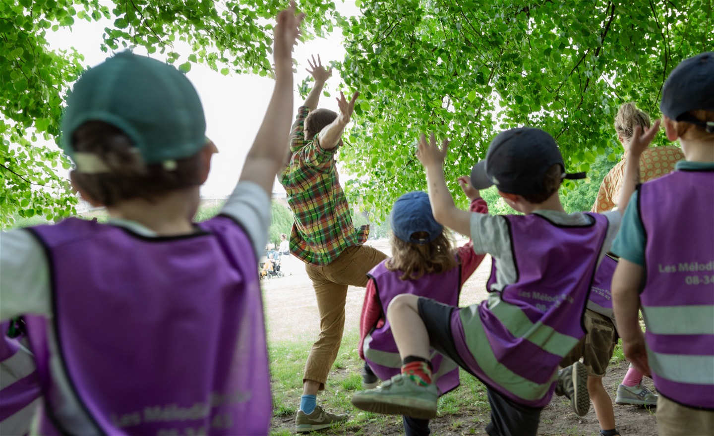 Barn som dansar utomhus i en dunge under lummiga gröna träd och löv.