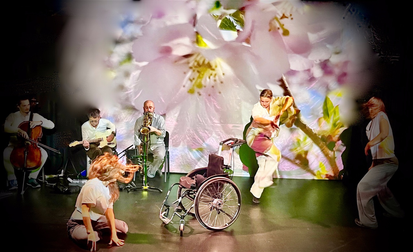 Tre dansare dansar och rör sig framför en filmprojektion med körsbärsblOmmor. Tre musiker spelar live (cello, gitarr, saxofon)