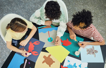 Tre personer skapar kollage med olikfärgade papper och figurer.