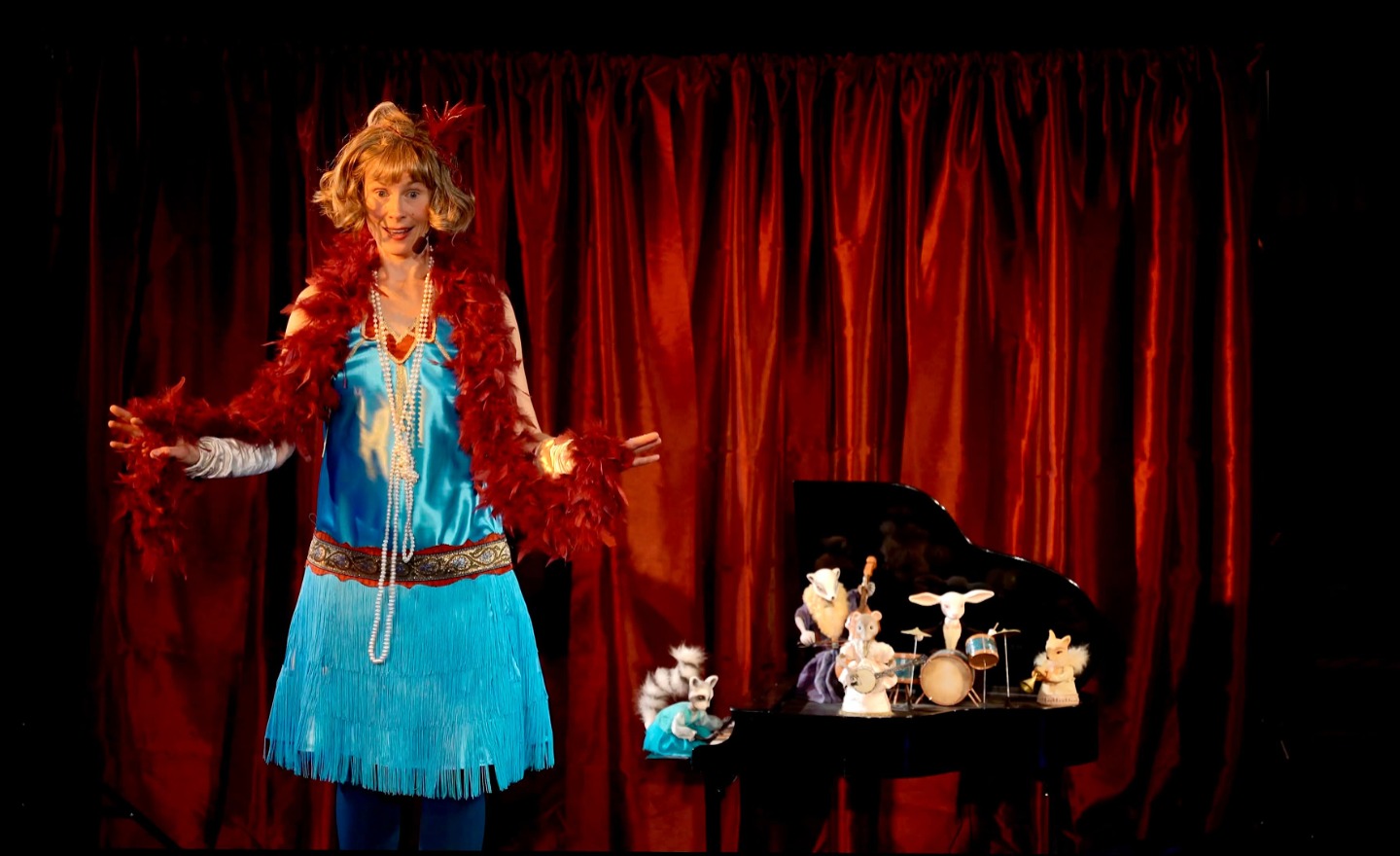 Micaela Gustafsson i turkos Charleston-outfit står bredvid en liten flygel med dockdjur med instrument på