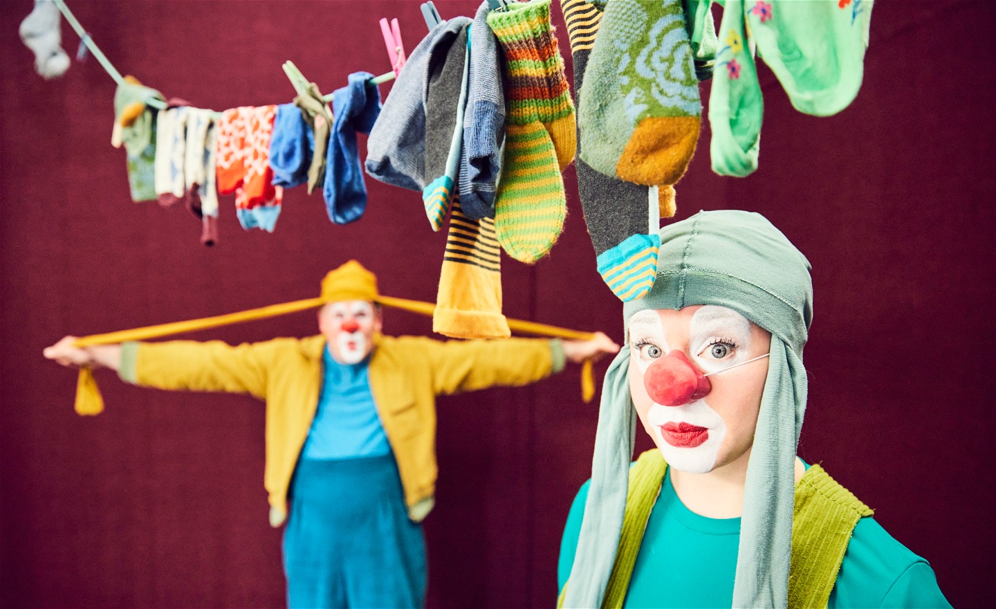 Två clowner i färgglada kläder under en tvättlina full med strumpor i olika färg och form.