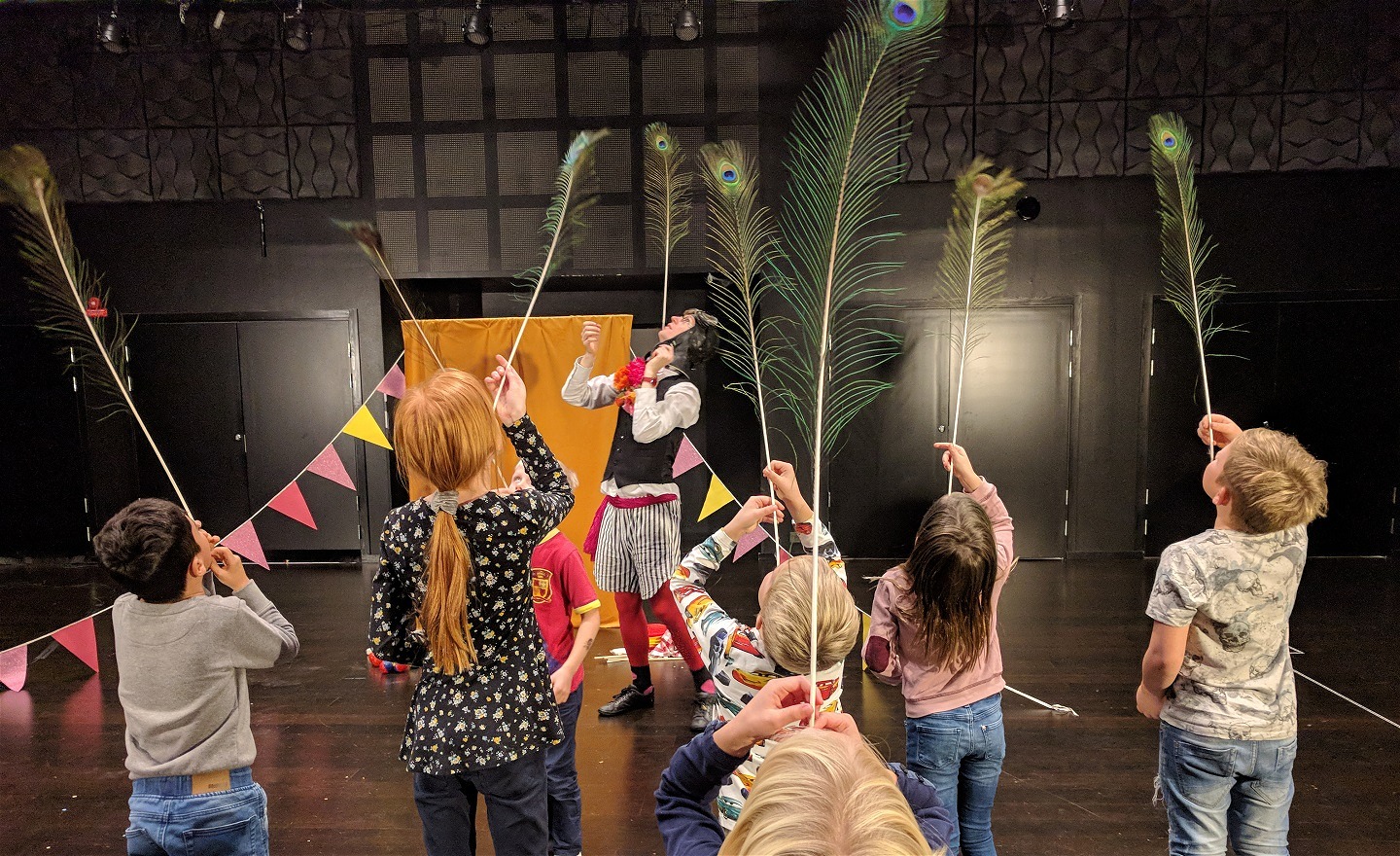 En bild på en clown och en grupp barn som balanserar påfågelfjädrar på hakan