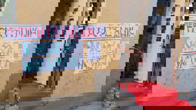 En röd matta leder in genom en dörr. På husfasaden finns en skylt med texten 