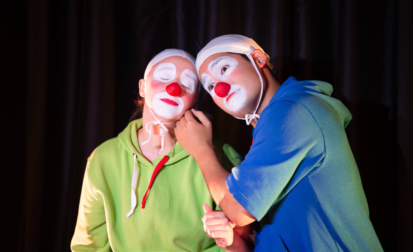 En clown i grön tröja stryks på kinden av en clown i blå tröja. 