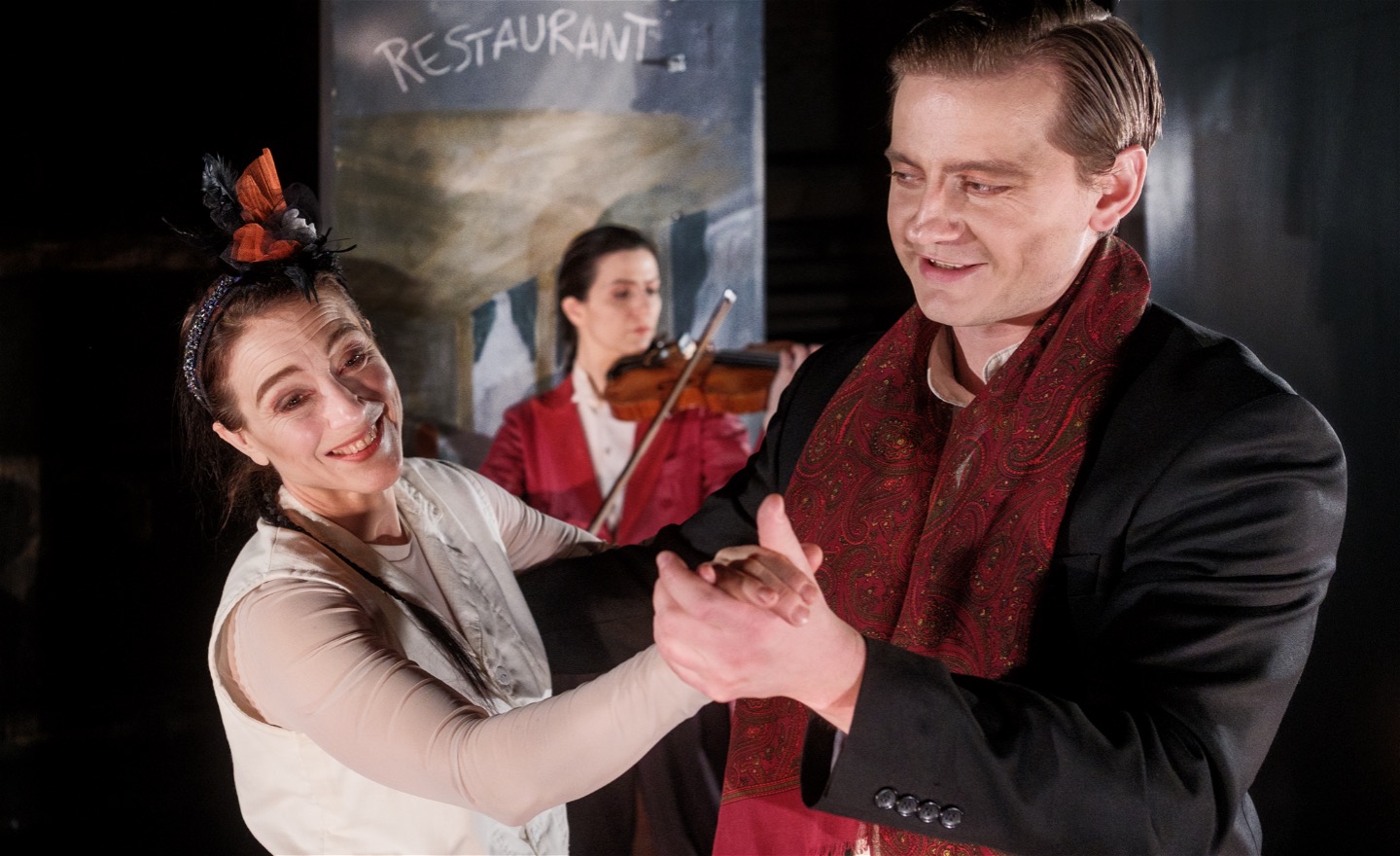 En violinist spelar och en kvinna och en man dansar till musiken, glada.