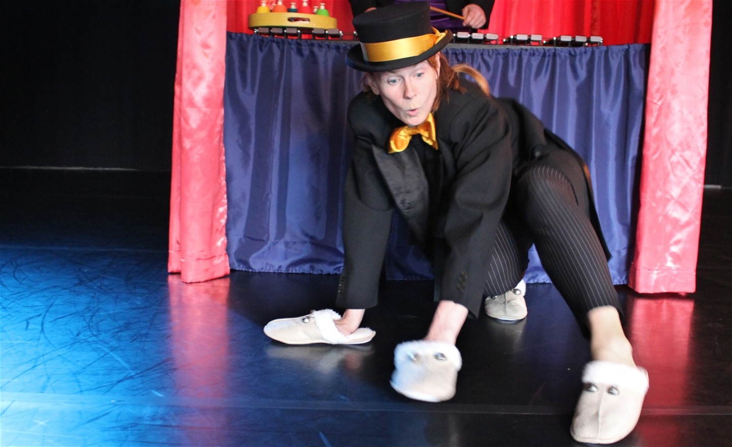 Micaela krypdansar på golvet iförd fårtofflor med pinglor på både händer och fötter.  