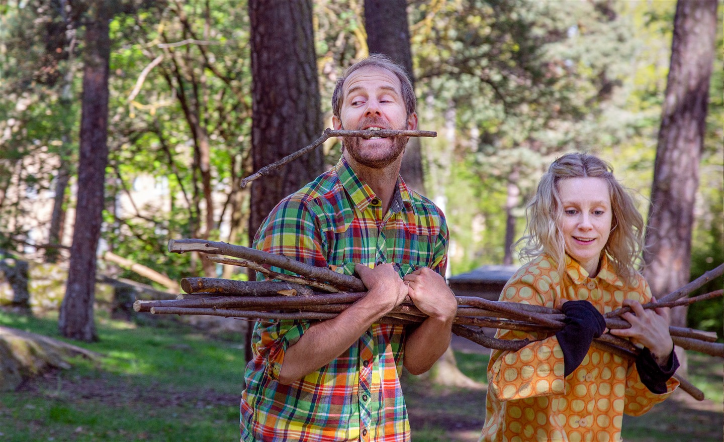 Två dansare, en man och en kvinna, bär gemensamt på en bunt med grenar. Mannen har en gren i munnen.