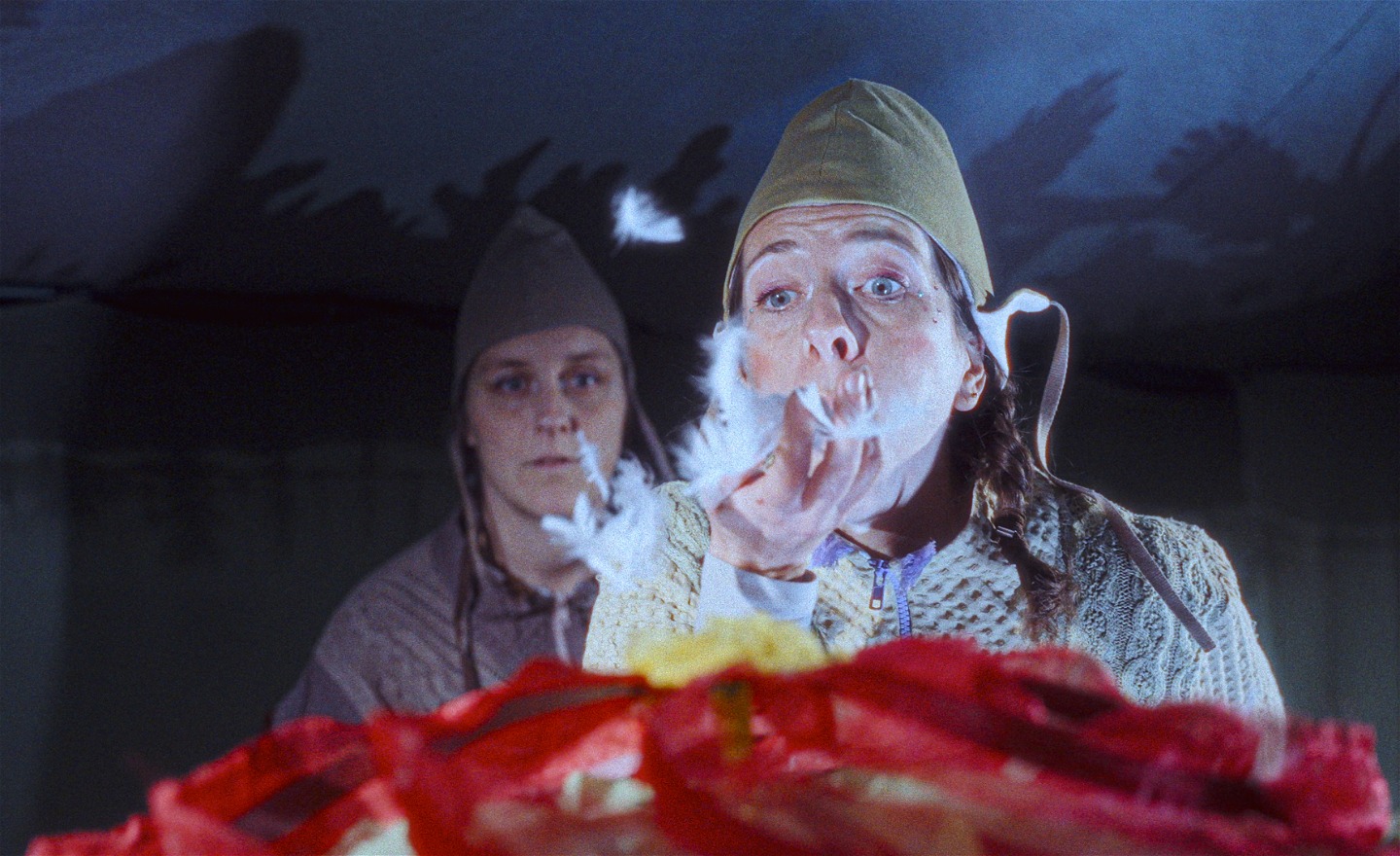 En skådespelerska i luva blåser vita fjädrar över en blomma