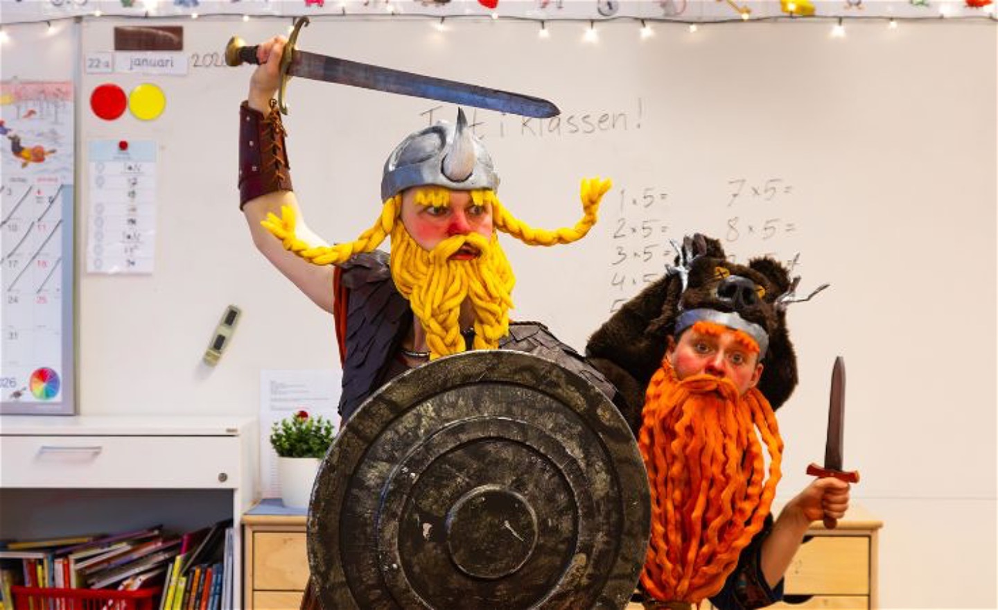 Två vikingar i ett klassrum. Den ena har en sköld och har rest sitt svärd. Den andra gömmer sig bakom med en dolk. 