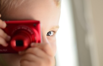 Barn i närbild håller upp kamera framför sitt öga