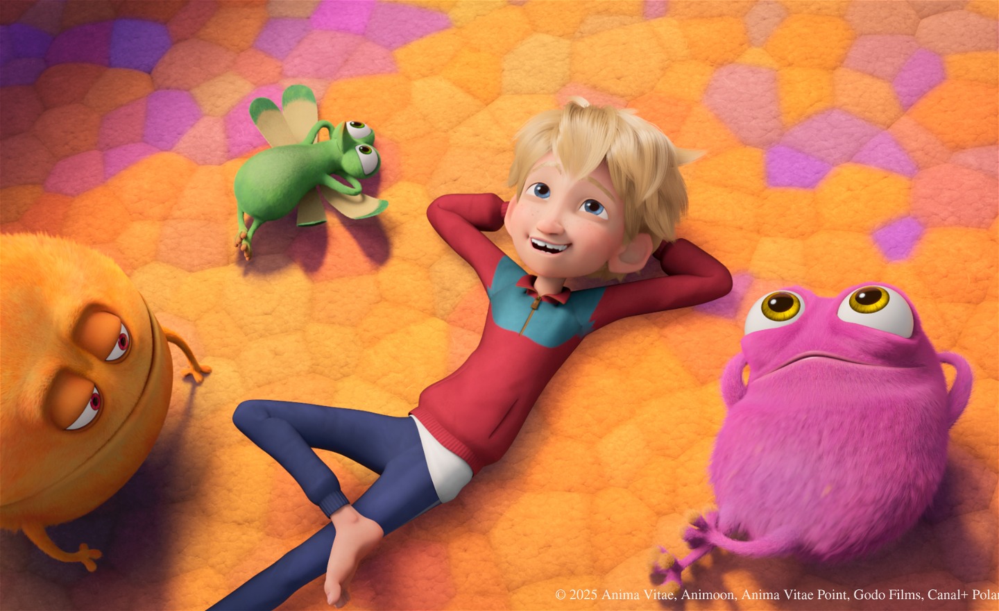 En glad pojke ligger på rygg på ett golv med färgglad heltäckningsmatta. Jämte honom finns tre fantasifigurer.