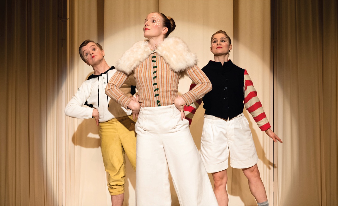 Tre dansare som står uppställda framför en ridå i en spotlight.