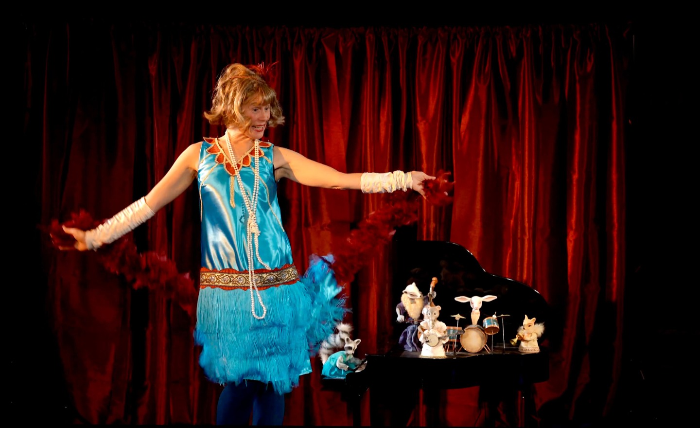 Micaela Gustafsson i turkos Charleston-outfit står bredvid en liten flygel med dockdjur med instrument på