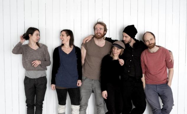 En grupp glada människor står lutade mot en vit vägg.