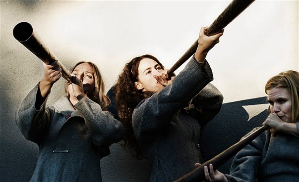 Tre personer blåser i instrument