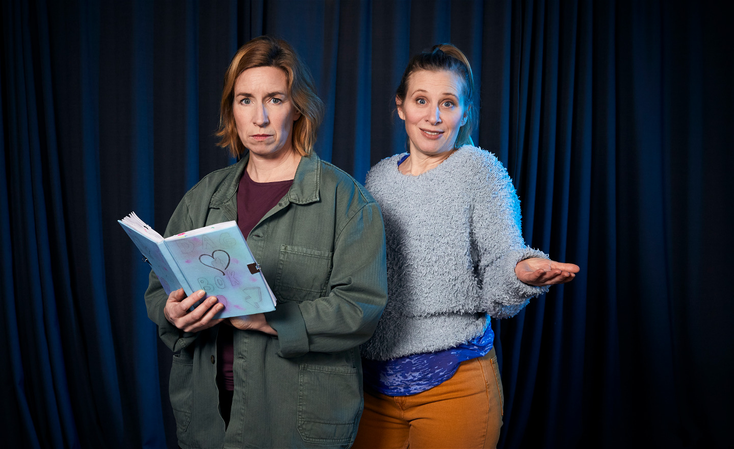 Bilden föreställer två skådespelare som tittar in i kameran. Den ena håller i en dagbok.