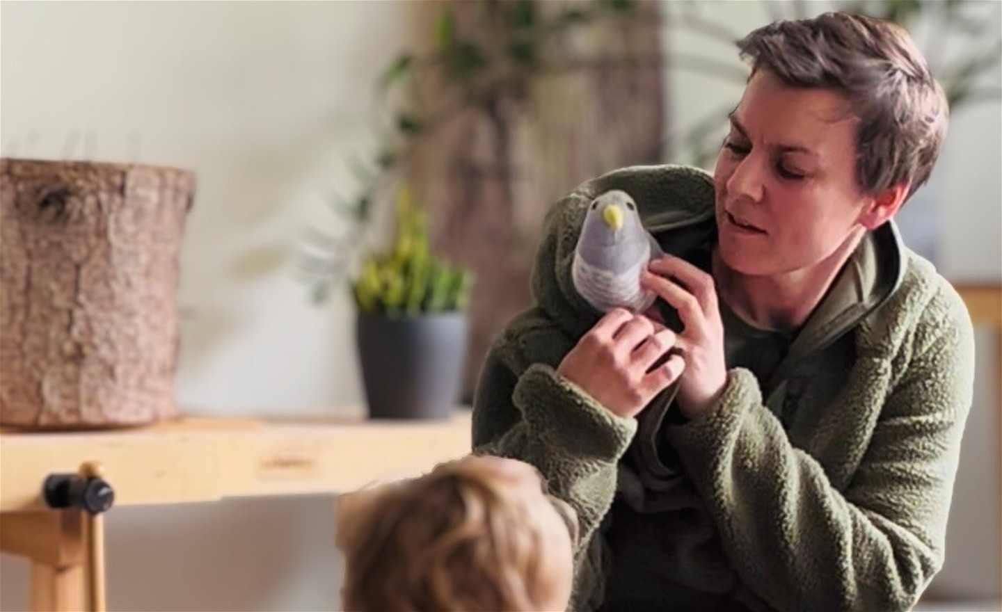 En person har en leksaksfågel i sin luva på jackan och visar den för ett barn. 