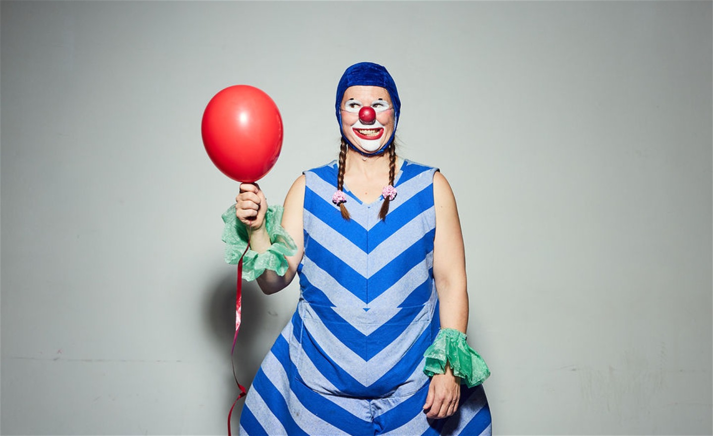 En clown som ser lurig ut håller en röd ballong.