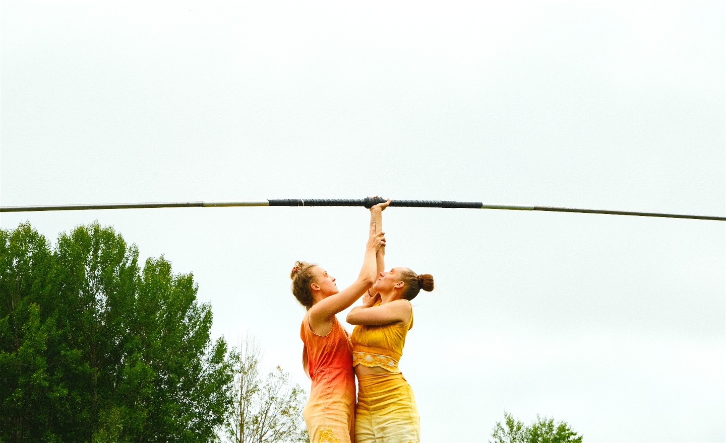 två kvinnor håller upp en lång järnstång mot himlen. 